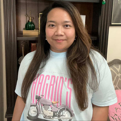 Person wearing a white t-shirt with a graphic design, standing in front of a shelf with various items.