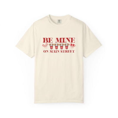 Beige t-shirt with red text 'BE MINE ON MAIN STREET' on a white background