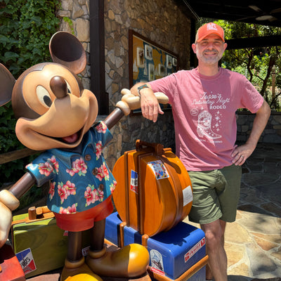 man in jesses saturday night rodeo tshirt standing with mickey mouse statue