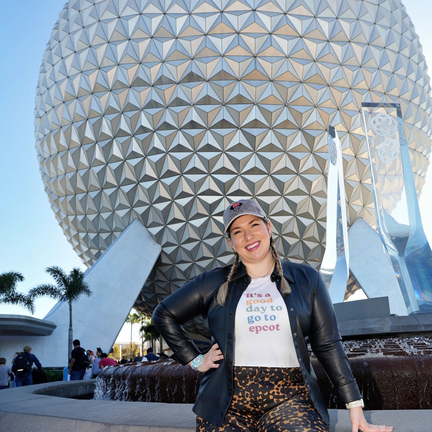 Person posing in front of a large, geometrically shaped structure with palm trees in the background.