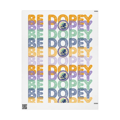 A vertical poster print featuring the word 'BE DOPEY' repeated in multiple pastel colors with a circular medallion containing a figure, alongside the phrase 'BE DOPEY' in matching lettering on a white background.