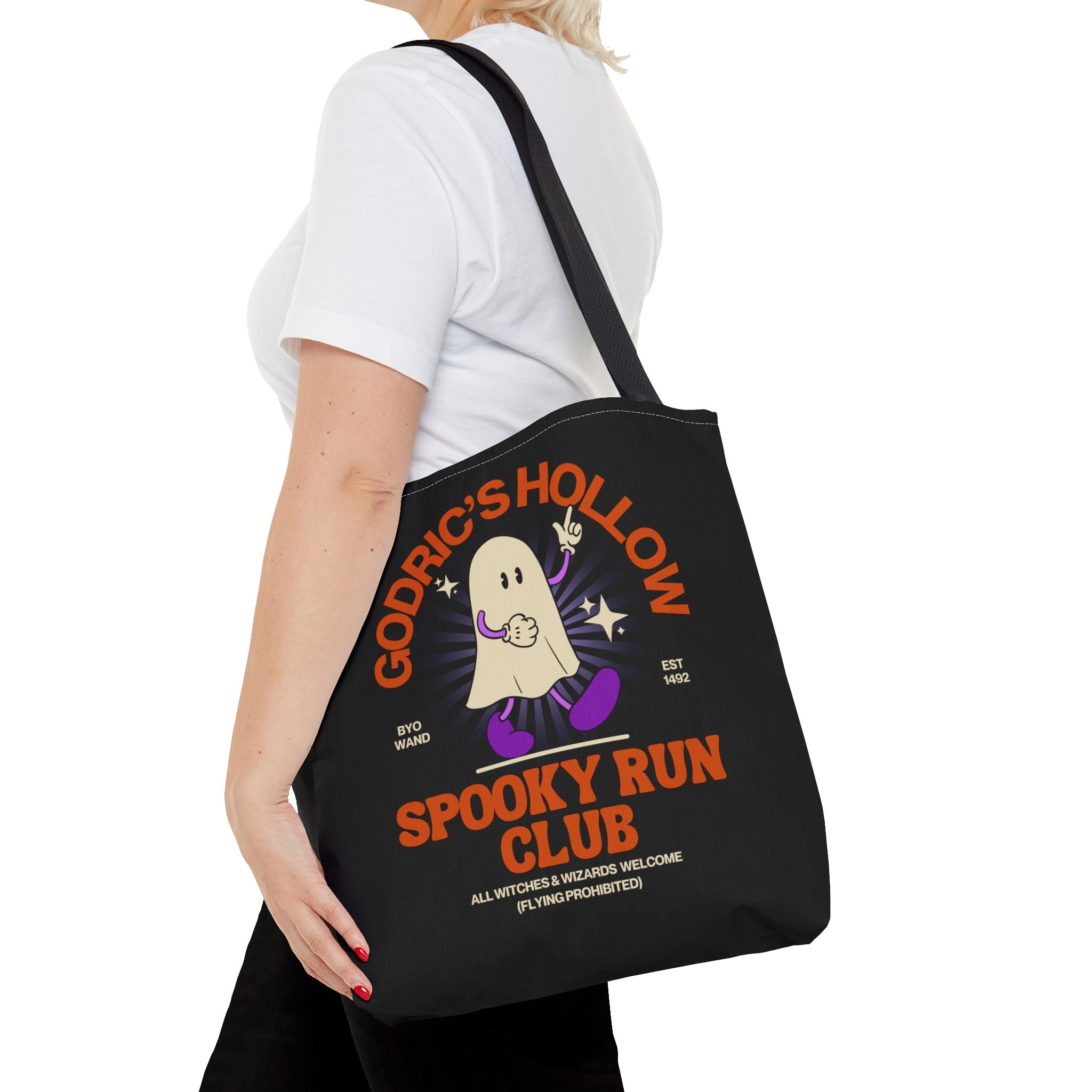 Person holding a black tote bag with 'Goddric's Hollow Spooky Run Club' design.