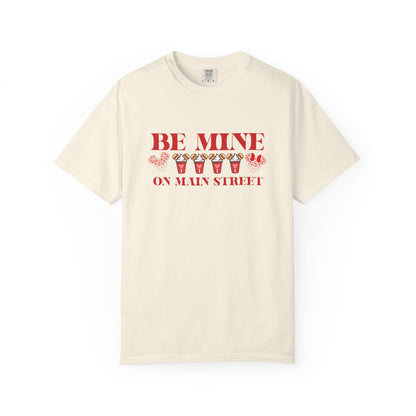 Beige t-shirt with red text 'BE MINE ON MAIN STREET' on a white background
