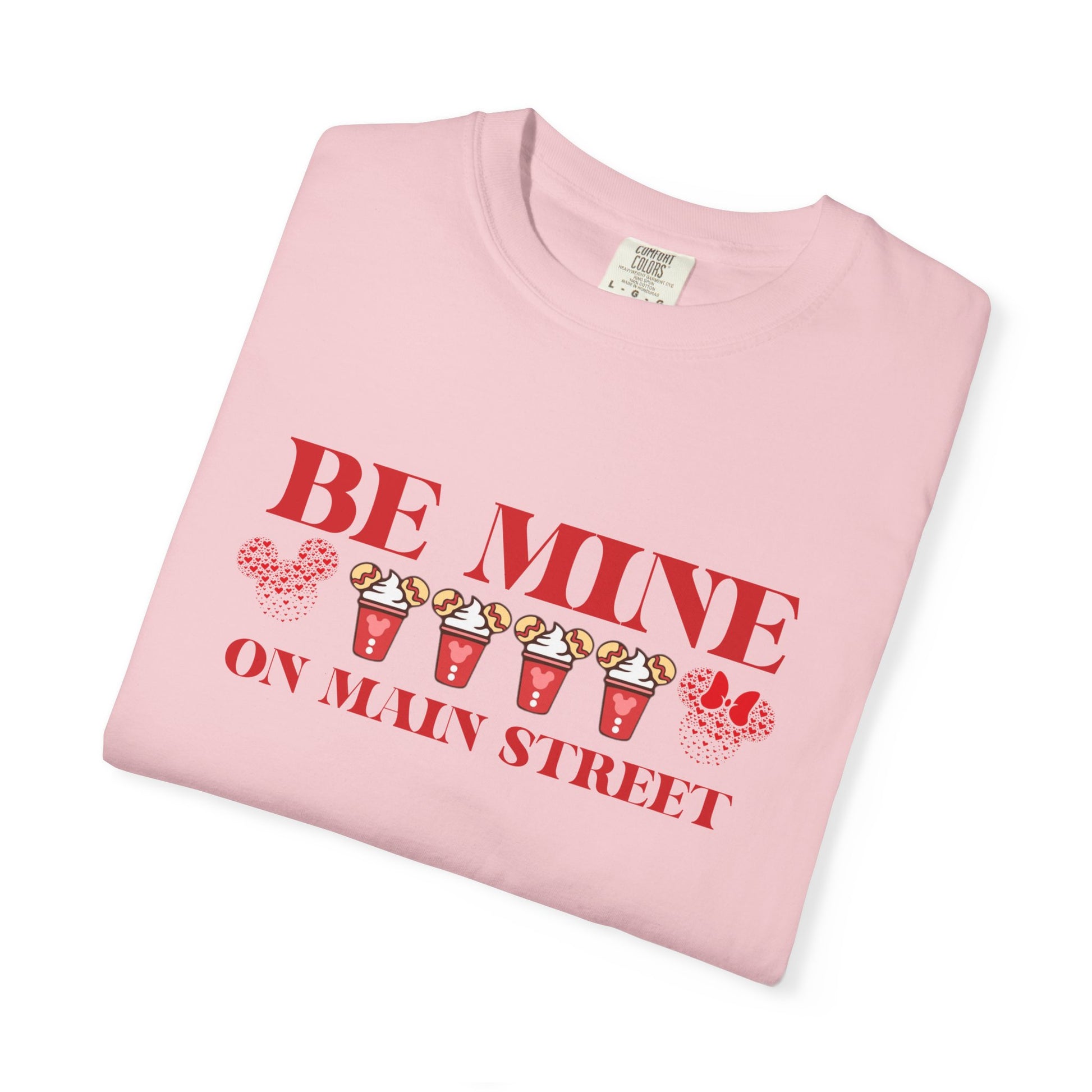Folded pink t-shirt with 'Be Mine on Main Street' text and graphics on a white background
