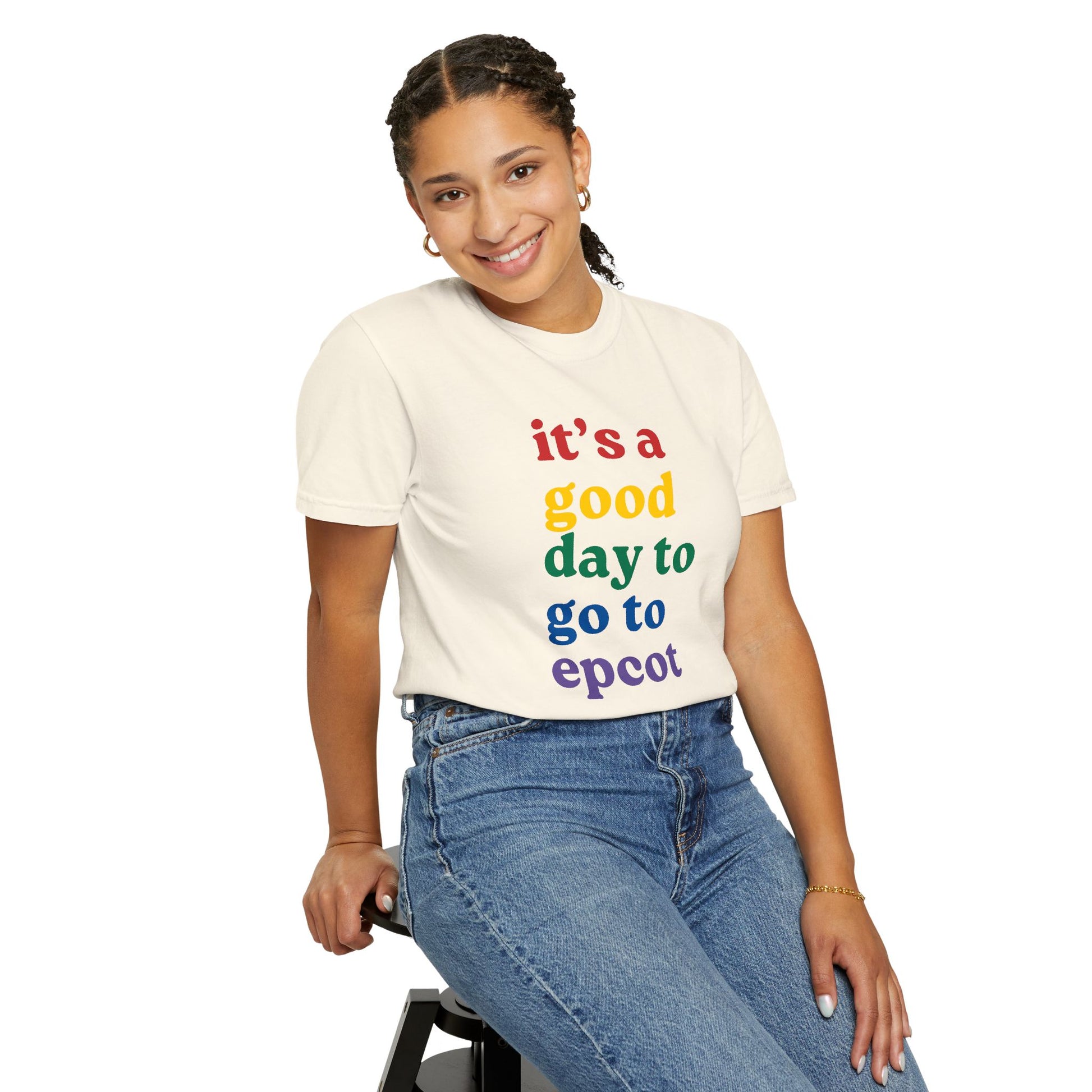 Person wearing a cream t-shirt with colorful text sitting on a stool against a white background
