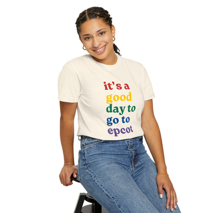 Person wearing a cream t-shirt with colorful text sitting on a stool against a white background