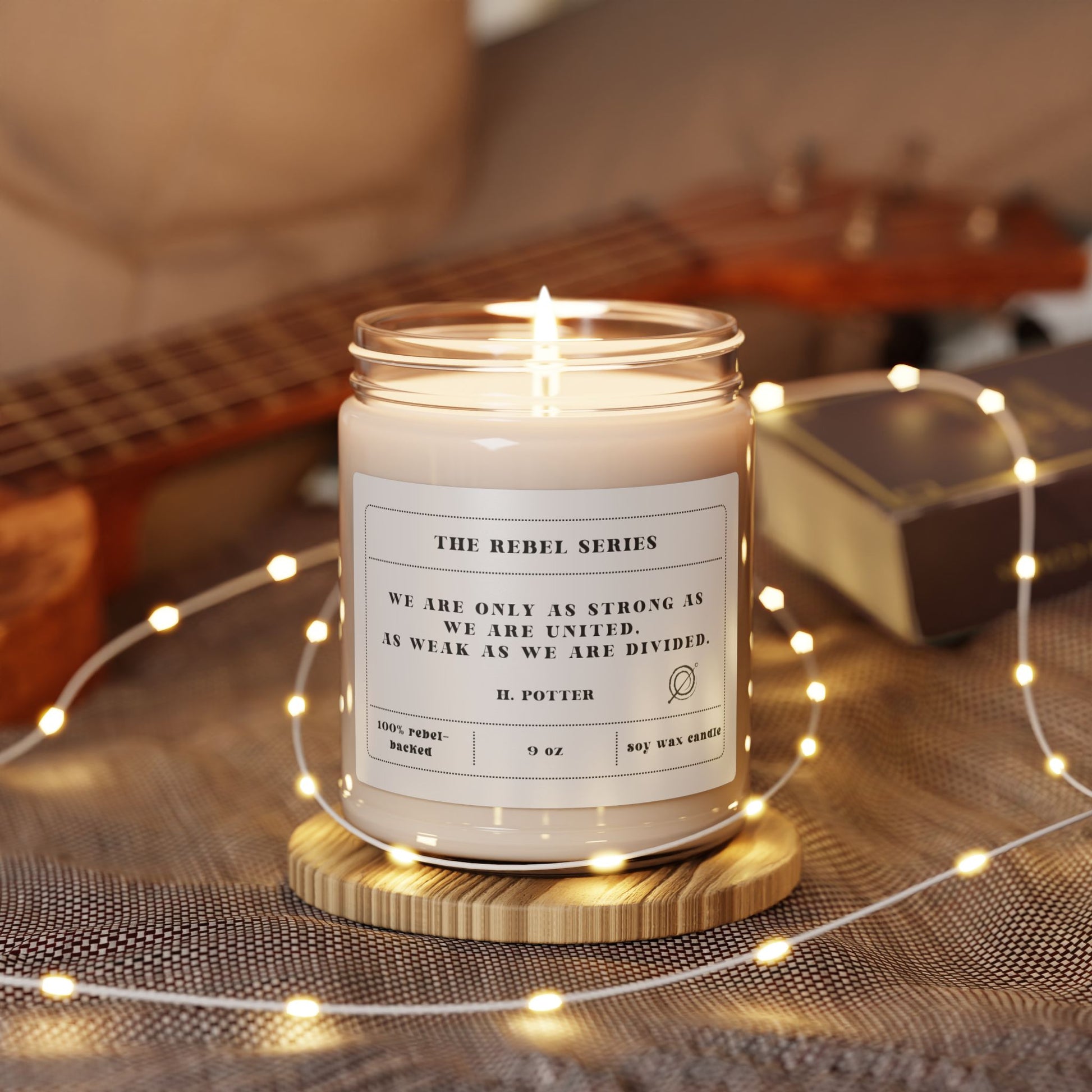Lit candle in a glass jar with a quote label, surrounded by string lights and a guitar in the background.