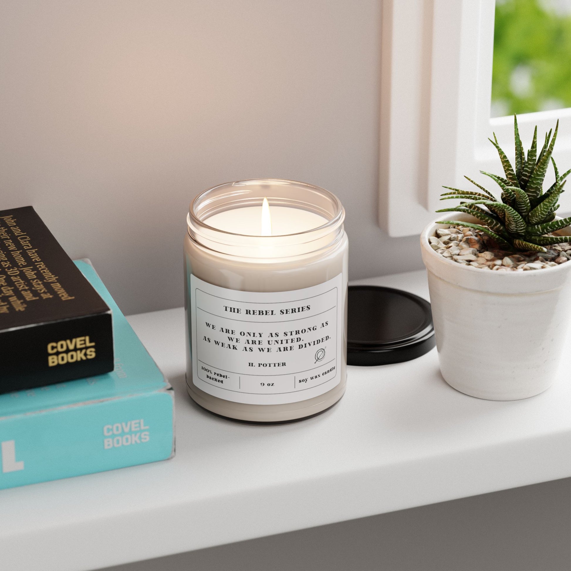 Candle in a glass jar with a label, books, and a plant on a shelf.