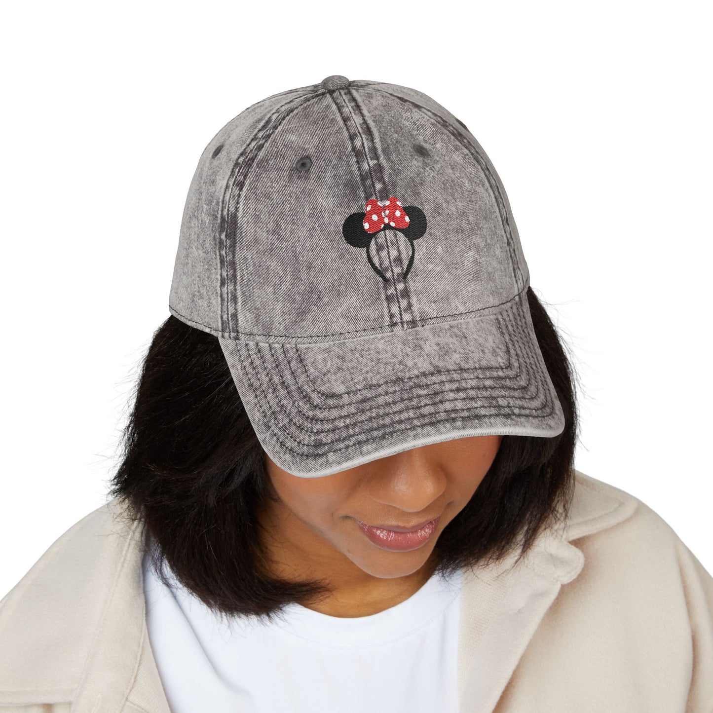 Person wearing a gray denim cap with a Minnie Mouse design on a white background