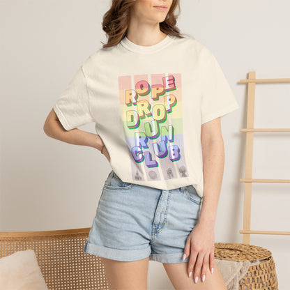 Person wearing a pride cream t-shirt with colorful text design and denim shorts in a casual setting.